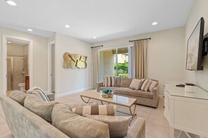 A modern living room with a sofa set, a coffee table, and a TV mounted on the wall. - 8BR near Disney | Pool, spa & game room (Kissimmee)