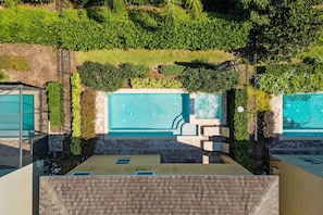 A rooftop pool area with a clear blue pool, surrounded by greenery and a brick wall. - 8BR near Disney | Pool, spa & game room (Kissimmee)