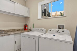 A laundry area with a double washer and dryer, a fire extinguisher, and a window with a view. - 4 suites near Disney | Balcony & covered patio (Kissimmee)