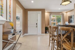 A modern kitchen with a dining area, featuring a white door, wooden chairs, and a small table with a vase of flowers. - 4 suites near Disney | Balcony & covered patio (Kissimmee)