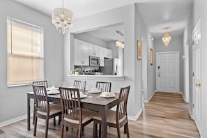 A dining area with a wooden table set for six, flanked by chairs, and a kitchen visible through an open doorway. - 4BR themed townhome near Disney | Lazy river (Davenport)