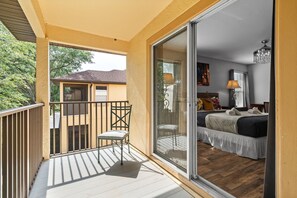 A balcony with a chair, a sliding glass door leading to a bedroom with a bed, a nightstand, and a lamp. - 4BR themed townhome near Disney | Lazy river (Davenport)