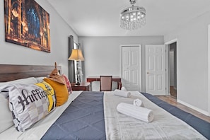 A hotel room with a bed, a desk, a chair, a lamp, a painting, and a chandelier. - 4BR themed townhome near Disney | Lazy river (Davenport)