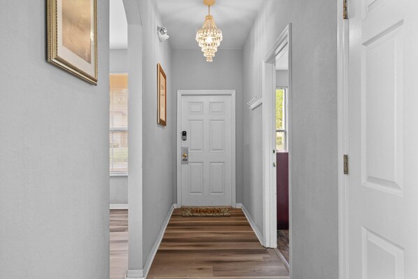 A hallway with a white door, a chandelier, and a framed picture on the wall. - 4BR themed townhome near Disney | Lazy river (Davenport)