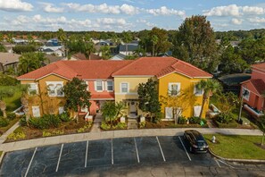 A multi-story residential building with a red-tiled roof, surrounded by greenery and a parking lot. - 3BR near Disney | Mickey & Harry Potter rooms (Kissimmee)