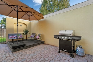 An outdoor patio with a grill, two chairs, an umbrella, and a potted plant. - 3BR near Disney | Mickey & Harry Potter rooms (Kissimmee)
