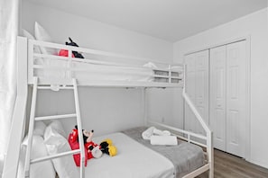 Ein Stockbett mit einer Leiter, ein kleines Bett im unteren Bereich und eine Tür rechts.