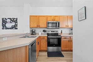 A modern kitchen with wooden cabinets, stainless steel appliances, and a black countertop. - 3BR near Disney | Mickey & Harry Potter rooms (Kissimmee)