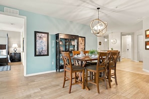 A dining area with a wooden table and chairs, a chandelier, and a bookshelf with framed pictures. - Vista Cay 4BR Condo • Lake View • Near Universal (Orlando)