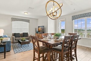 Uma sala de estar moderna com área de jantar, apresentando um candelabro, televisão e vista para o exterior.