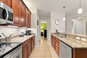 A modern kitchen with wooden cabinets, granite countertops, stainless steel appliances, and a visible clock on the wall. - Vista Cay 4BR Condo • Lake View • Near Universal (Orlando)