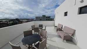 A rooftop terrace with a round table and wicker chairs, overlooking a cityscape. - Flat Studio no Centrinho de Porto (Ipojuca)