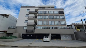 A multi-story building with a garage entrance, a white car parked inside, and a clear sky. - Flat Studio no Centrinho de Porto (Ipojuca)
