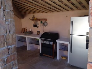 Een keuken met een stenen muur, een houten plafond, een witte koelkast en een ingebouwde grill.
