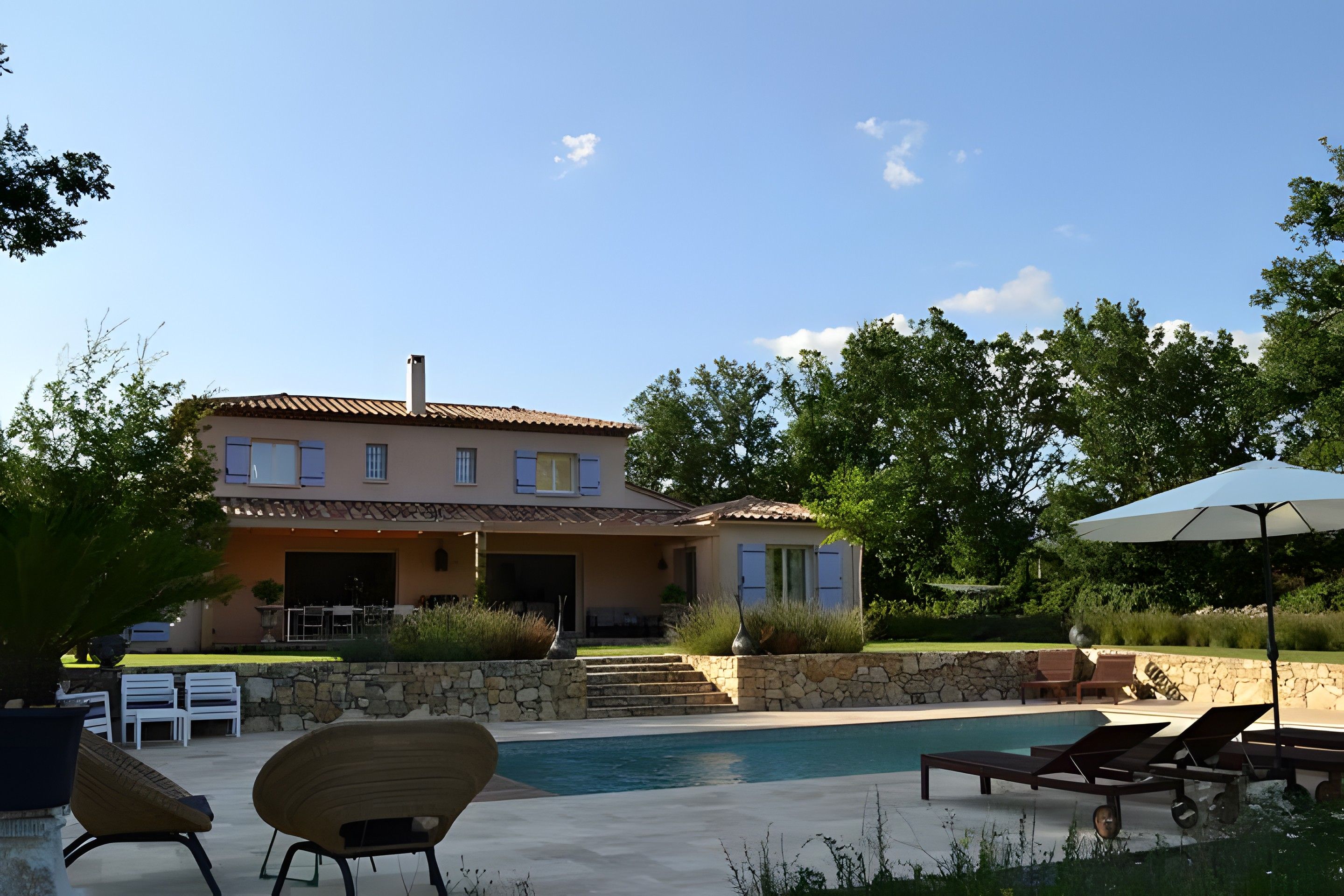 A two-story house with a swimming pool, outdoor seating, and a stone wall.