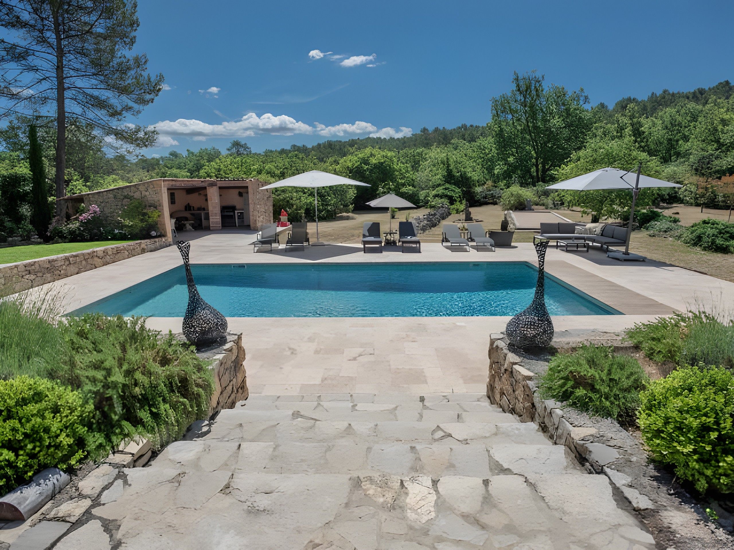 A swimming pool with a stone pathway leading to a seating area with umbrellas.