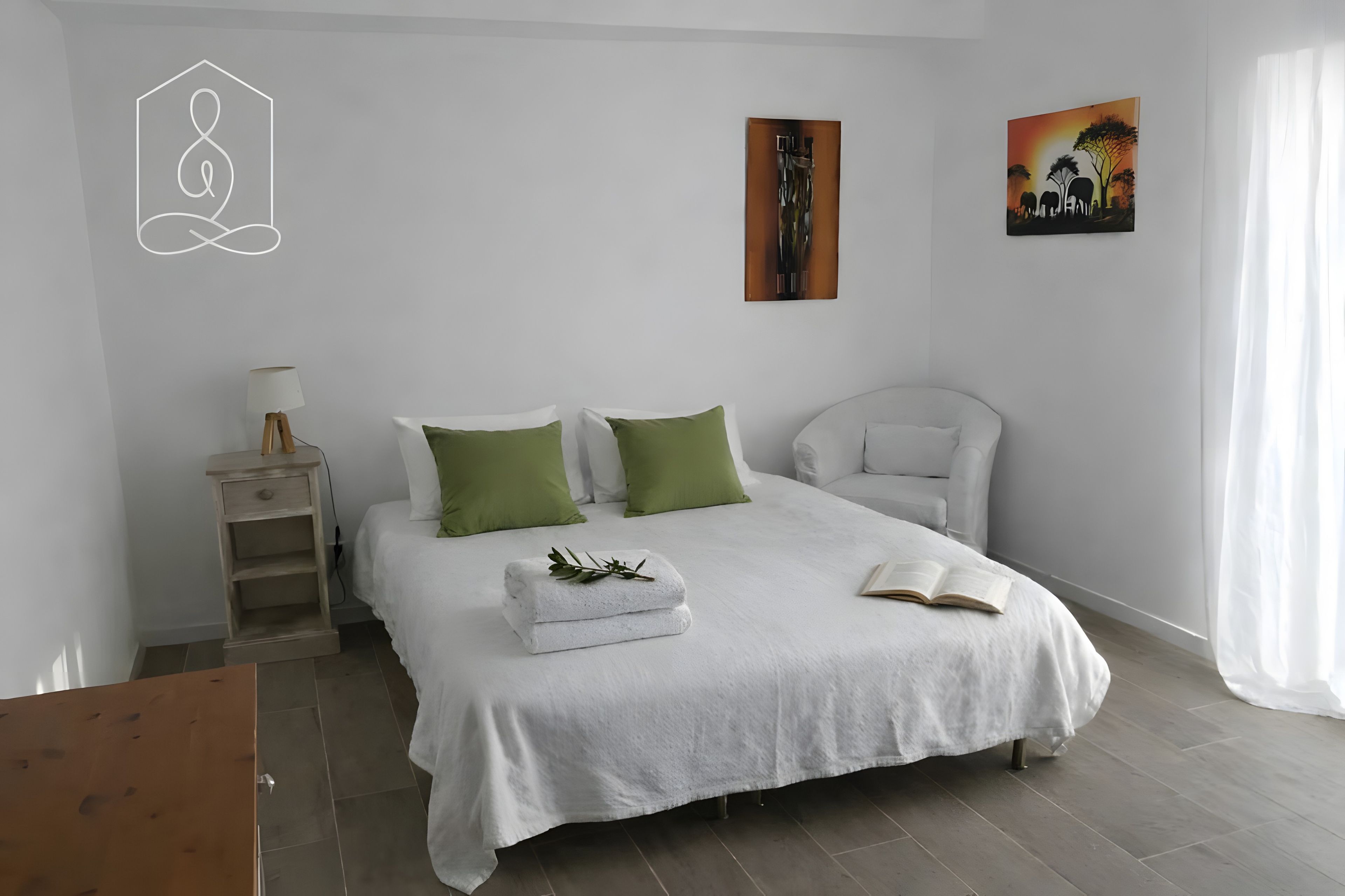 Een slaapkamer met een bed, kussens, een nachtkastje, een lamp en een schilderij aan de muur.