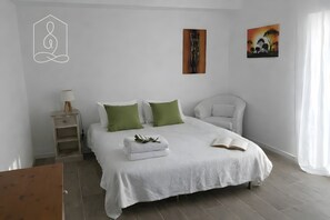 Een slaapkamer met een bed, kussens, een nachtkastje, een lamp en een schilderij aan de muur.