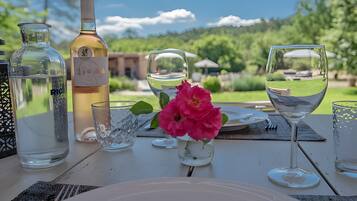A table set outdoors with a bottle of wine, glasses, and a flower centerpiece.