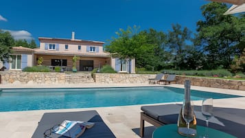 Un espace piscine avec des chaises longues et une table, un mur en pierre et une maison en arrière-plan.