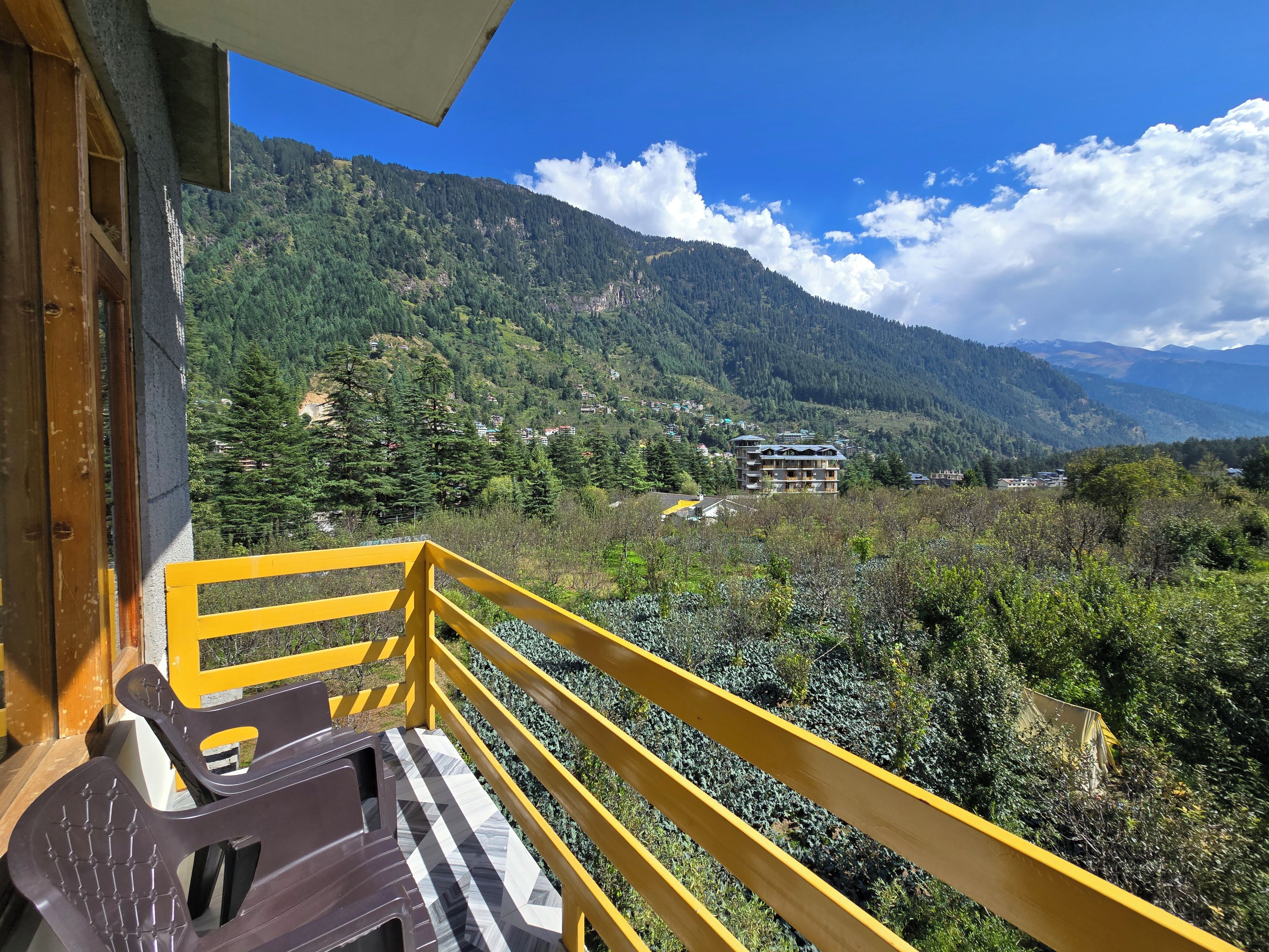 Un balcon doté d’une rambarde jaune, qui offre une vue sur un paysage montagneux parsemé de bâtiments.