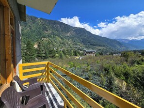 A balcony with a yellow railing overlooking a mountainous landscape with buildings. - The Cow Boy Manali (Manali)