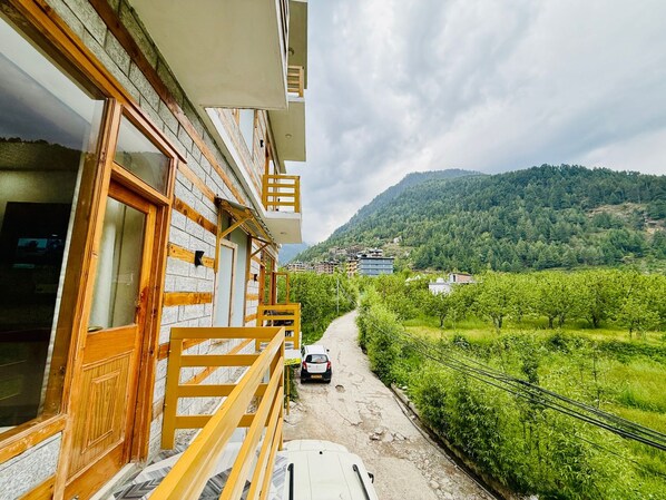 A building with a balcony overlooking a rural landscape with a road and greenery.