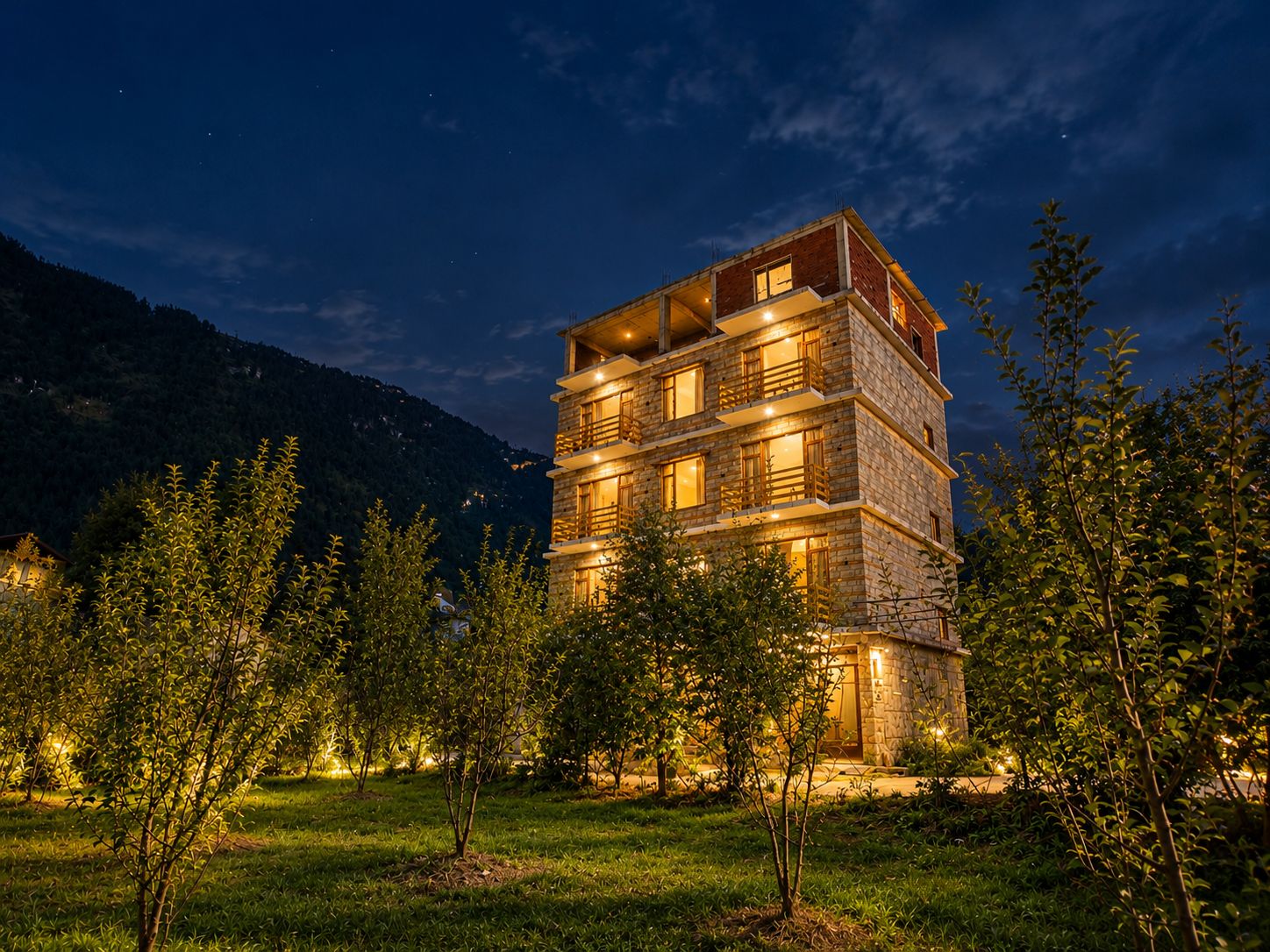 Un immeuble à plusieurs étages, doté de balcons, entouré d’arbres et ayant une chaîne de montagnes en toile de fond.