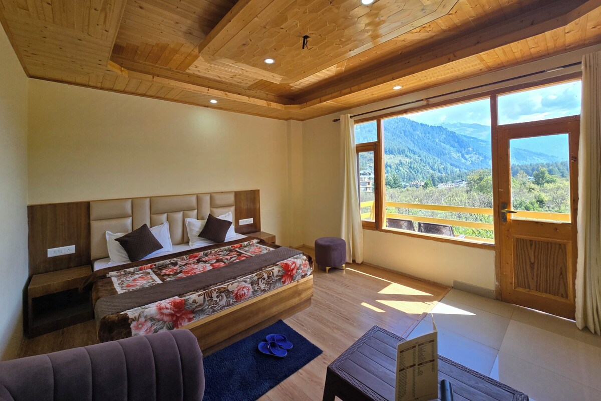 A bedroom with a large bed, a wooden ceiling, and a window with a mountain view.