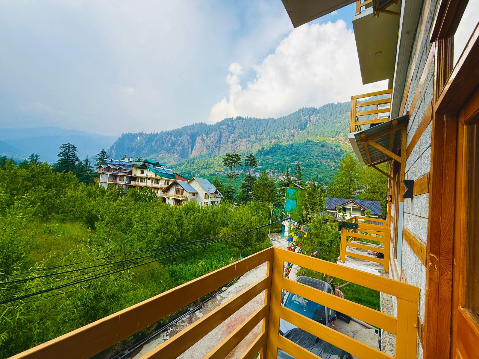 Een balkon met uitzicht op een bergachtig landschap, een houten hekwerk en een gebouw met meerdere verdiepingen.