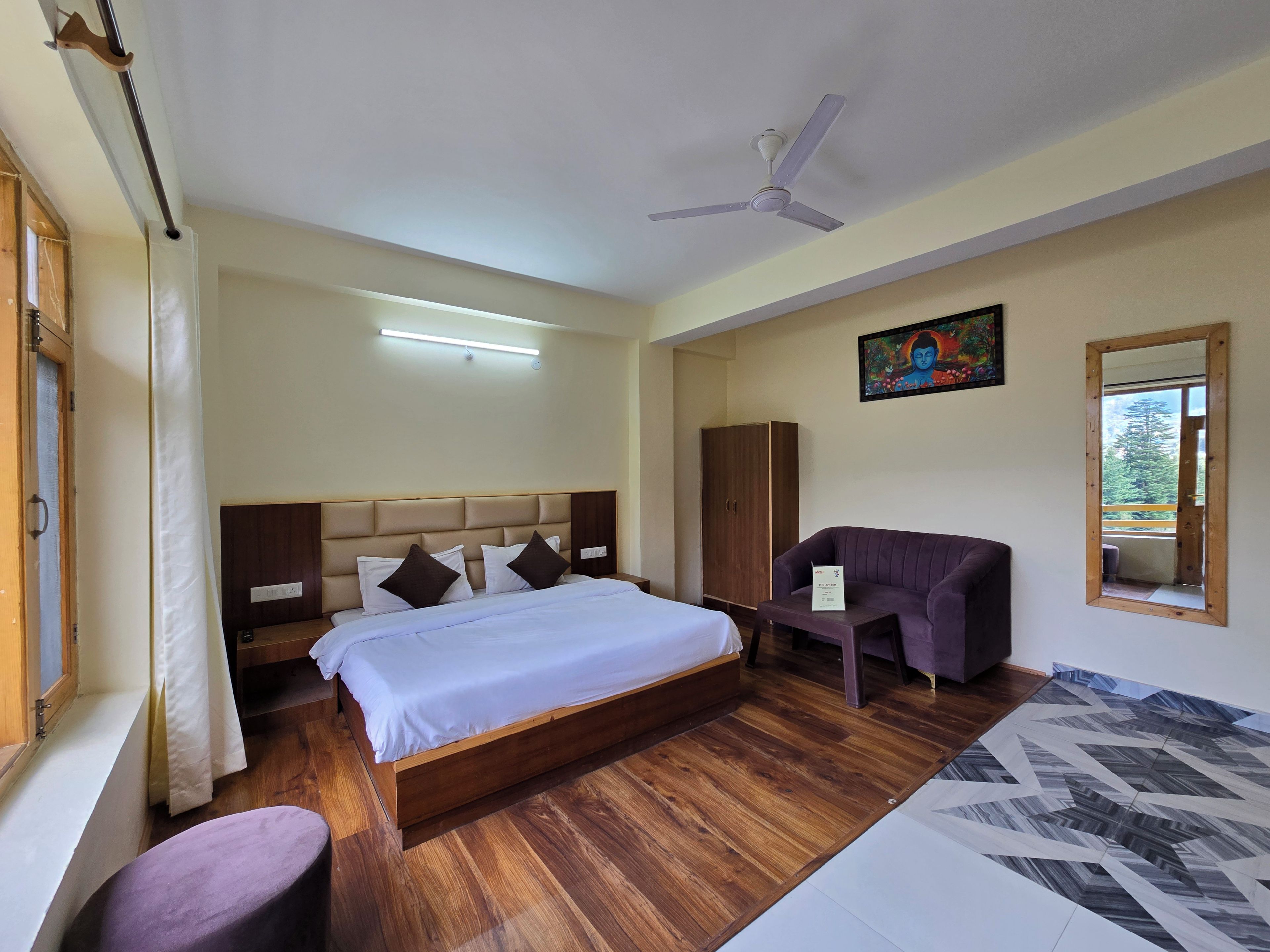 A hotel room with a bed, a seating area, a wardrobe, and a ceiling fan.