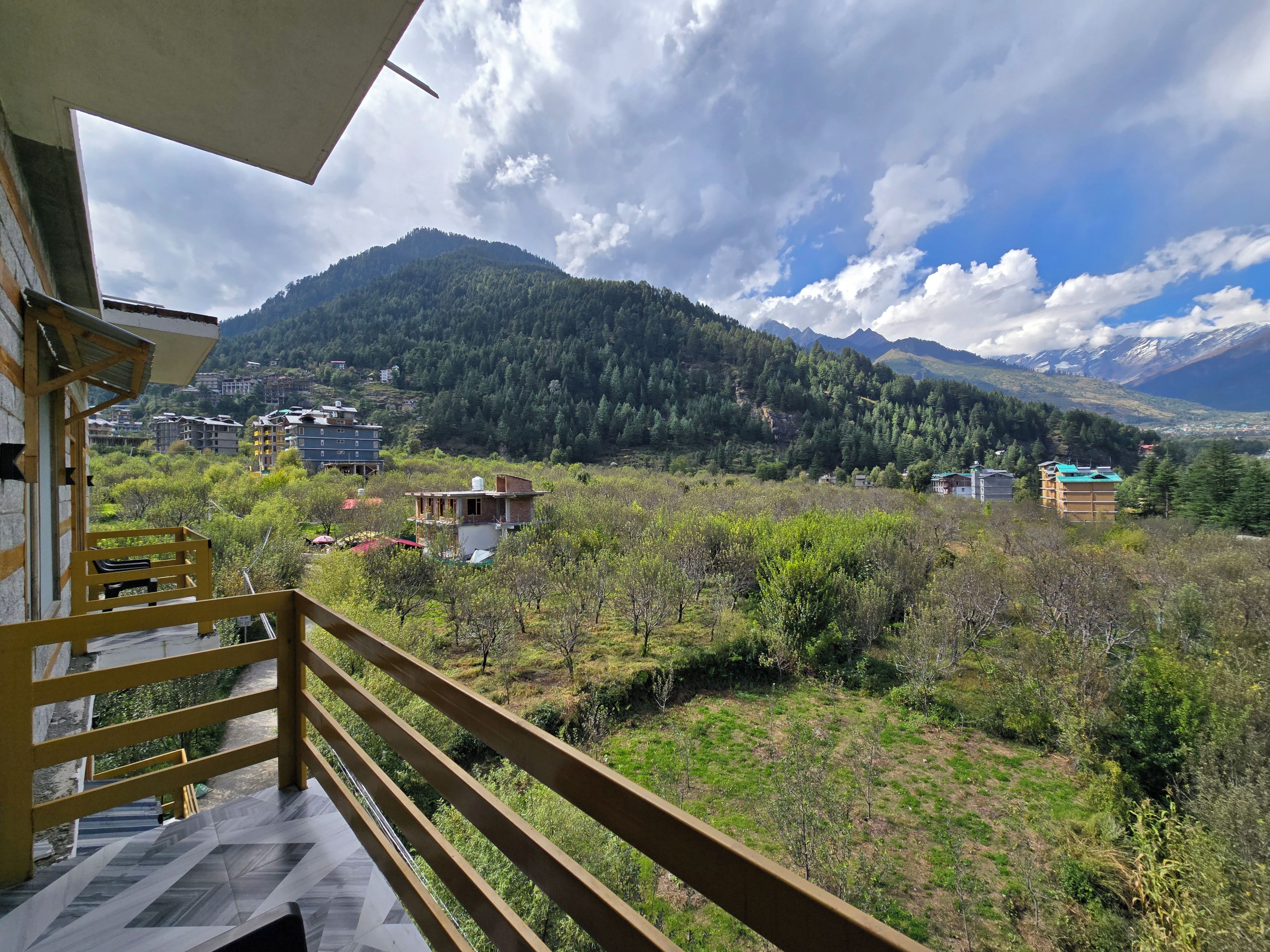 A balcony with a view of a mountainous landscape, a building with a green roof, and a clear sky.