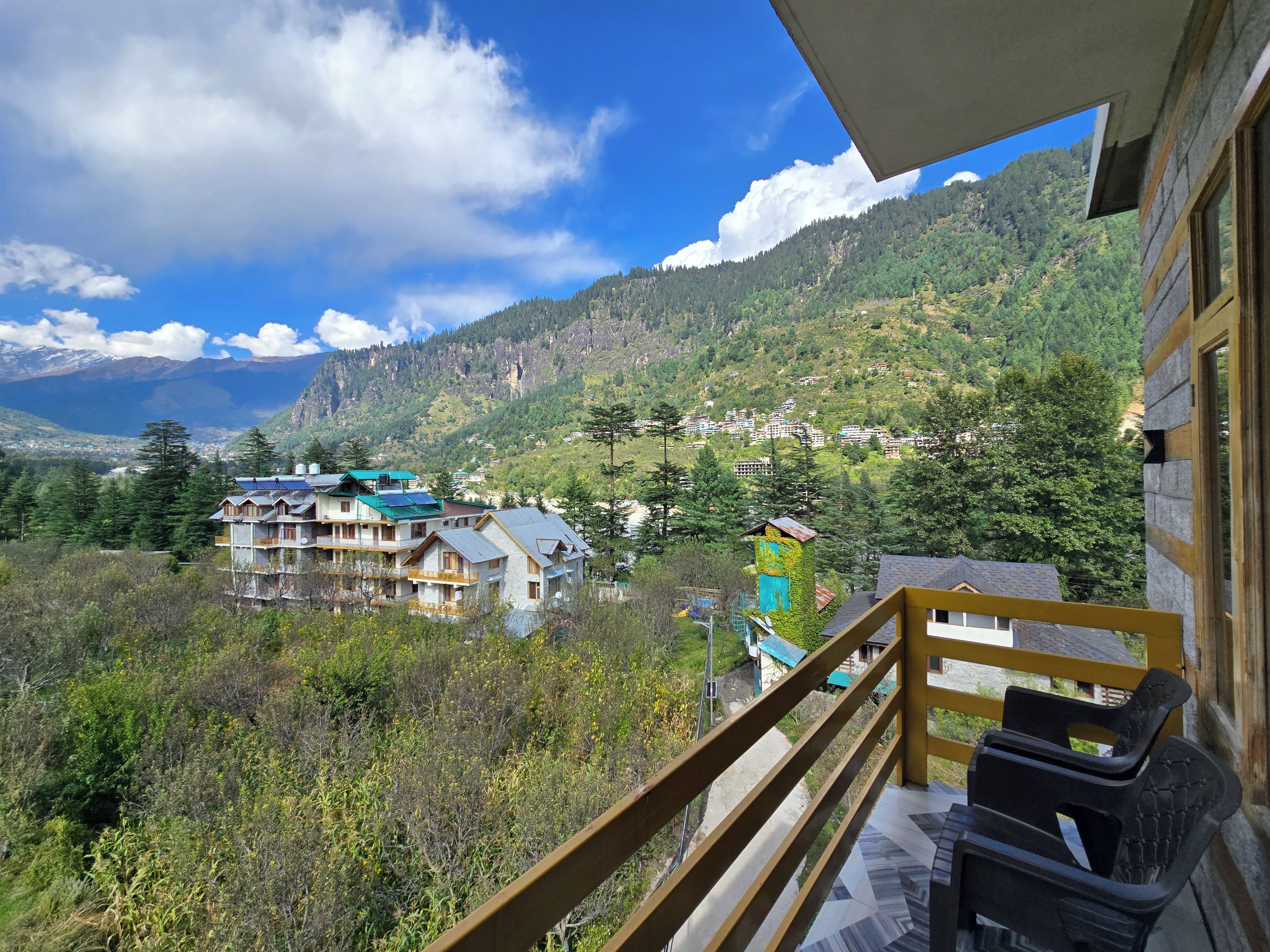Ein Balkon mit Blick auf eine gebirgige Landschaft, ein mehrstöckiges Gebäude und ein klarer Himmel.