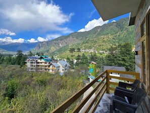 A balcony with a view of a mountainous landscape, a building with multiple floors, and a clear sky.