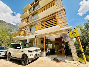 A multi-story building with a glass entrance, a sign for 'The Cowboy Inn,' and a white SUV parked in front. - The Cow Boy Manali (Manali)