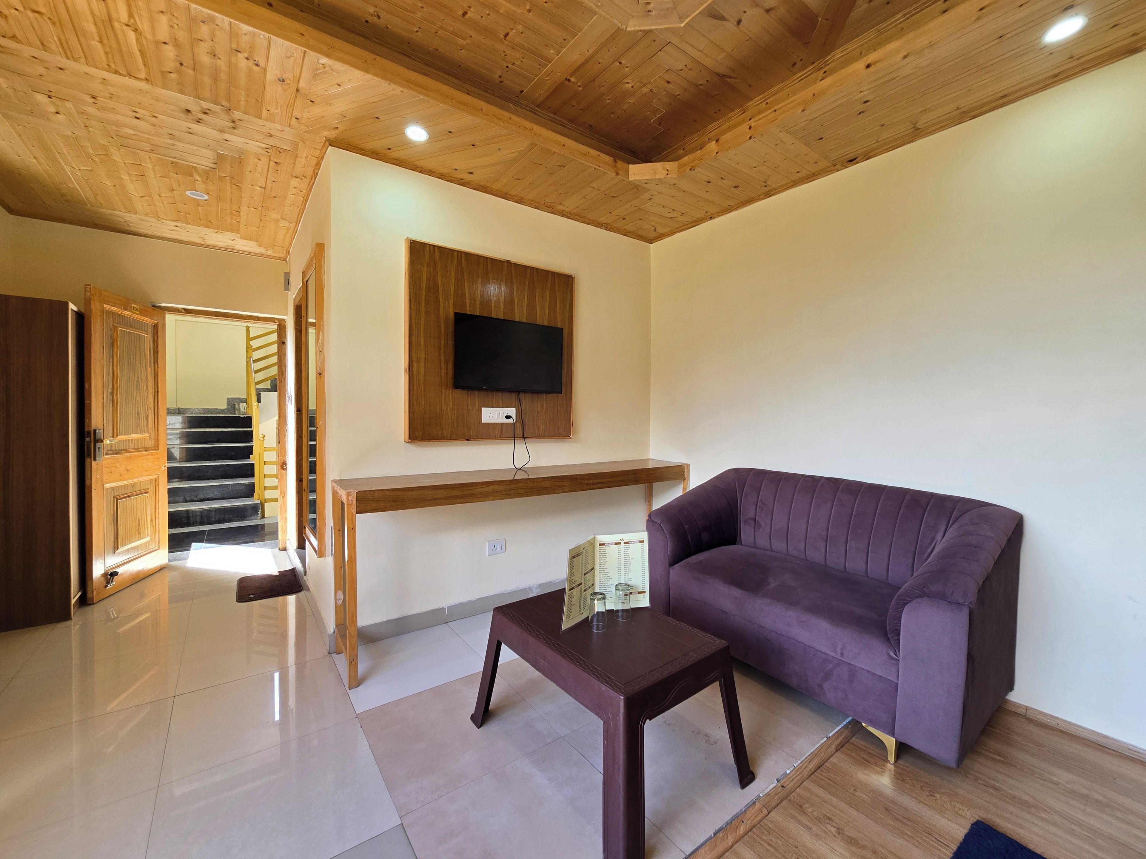 Un salon avec un plafond en bois, un canapé violet, une table basse en bois et un téléviseur à écran plat fixé au mur.