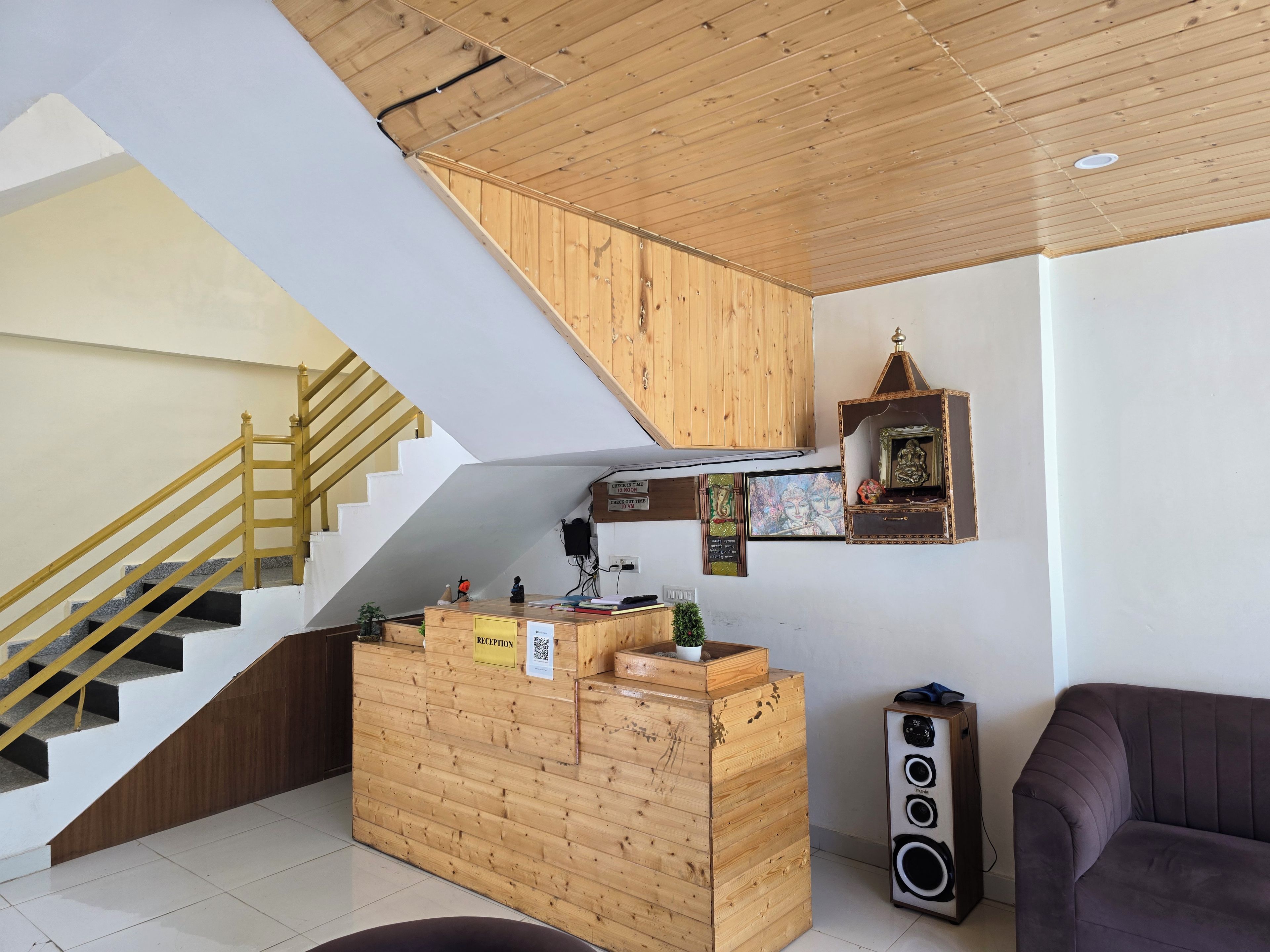Un comptoir d’accueil avec un revêtement en bois, un escalier doté d’une rampe jaune et un haut-parleur fixé au mur.