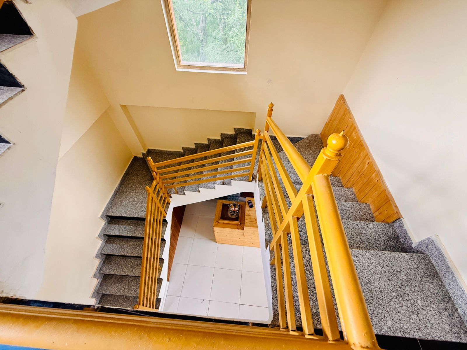 Un escalier avec une rampe, une petite plateforme avec une table, et une fenêtre donnant sur les arbres.