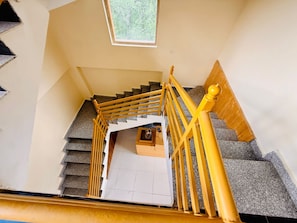A staircase with a handrail, a landing with a small table, and a window with a view of trees. - The Cow Boy Manali (Manali)