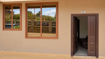 A building entrance with a flat entrance door, a sign indicating 'FLAT 2', and a view of a parking area with cars and greenery outside.