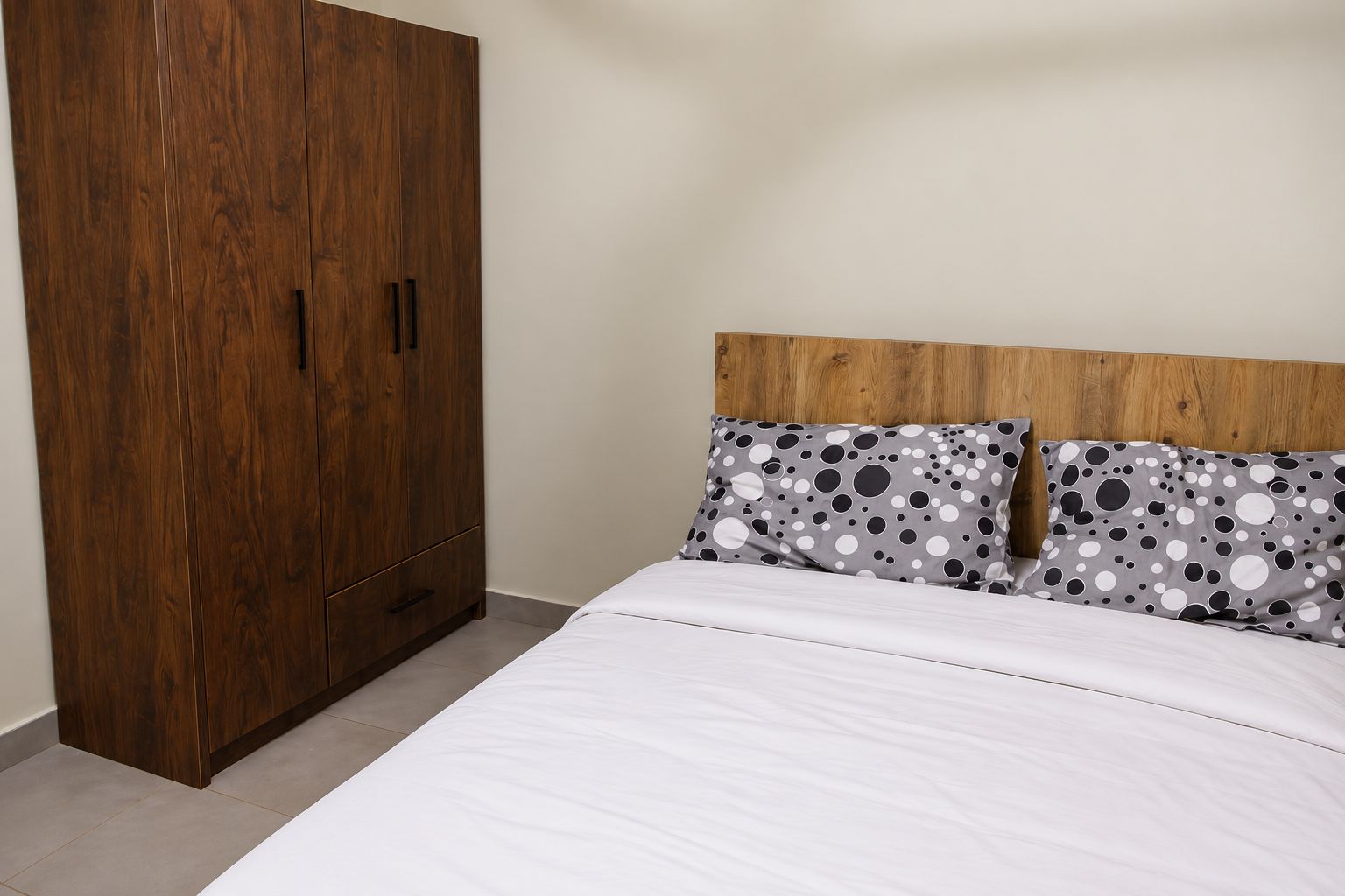 A bedroom with a wooden wardrobe, a bed with white bedding, and two pillows with a polka dot pattern.
