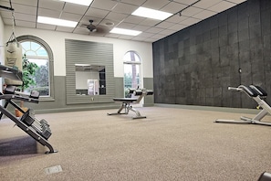 Een sportschool met trainingsapparatuur, grote ramen en uitzicht op de omgeving.