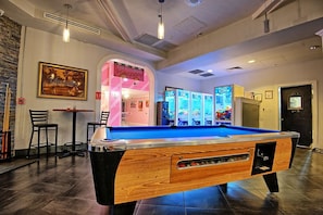 Een pooltafel in een ruimte met een bar, automaten en een neonreclame.