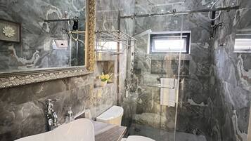 A bathroom with a marble wall, a large sink, a toilet, and a glass-enclosed shower area.