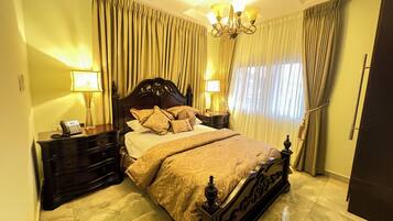 A bedroom with a large bed, two bedside tables with lamps, a chandelier, and curtains.