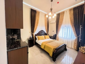 A hotel room with a bed, bedside table, and a desk with a chair. - AfriBella Luxury Suite (Kumasi)