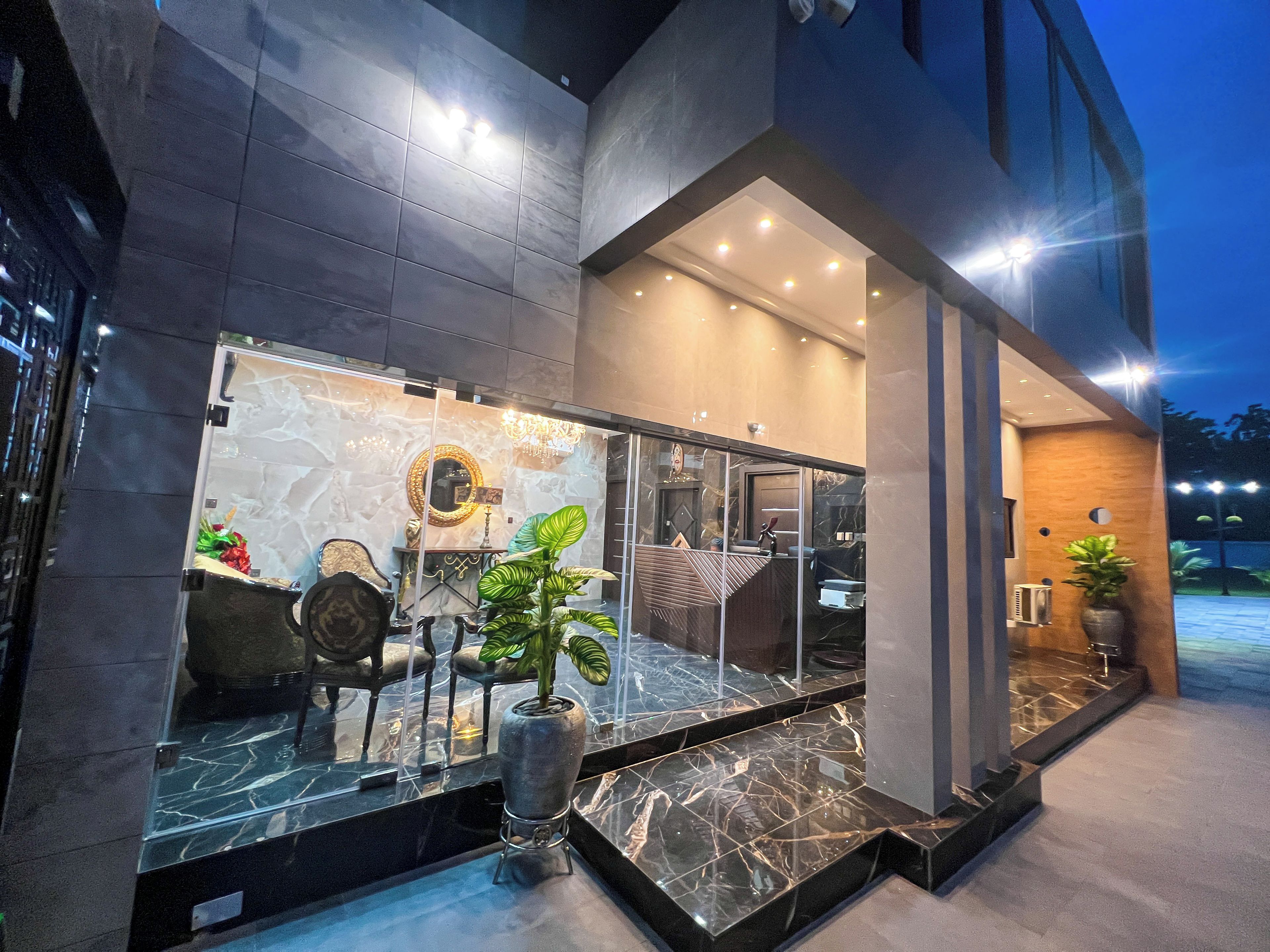 A modern hotel entrance with a glass facade, marble flooring, and a chandelier.