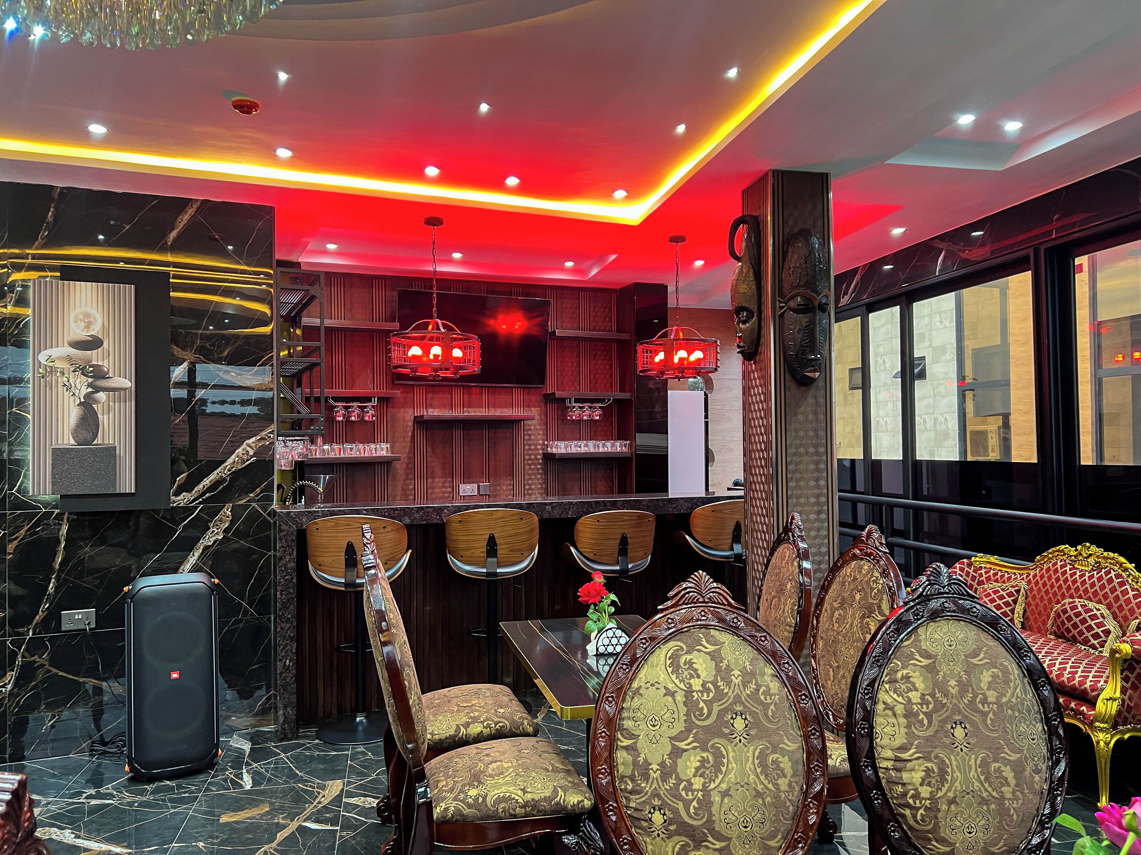 Un espace bar avec des chaises en bois, une valise noire et un éclairage d’ambiance rouge.