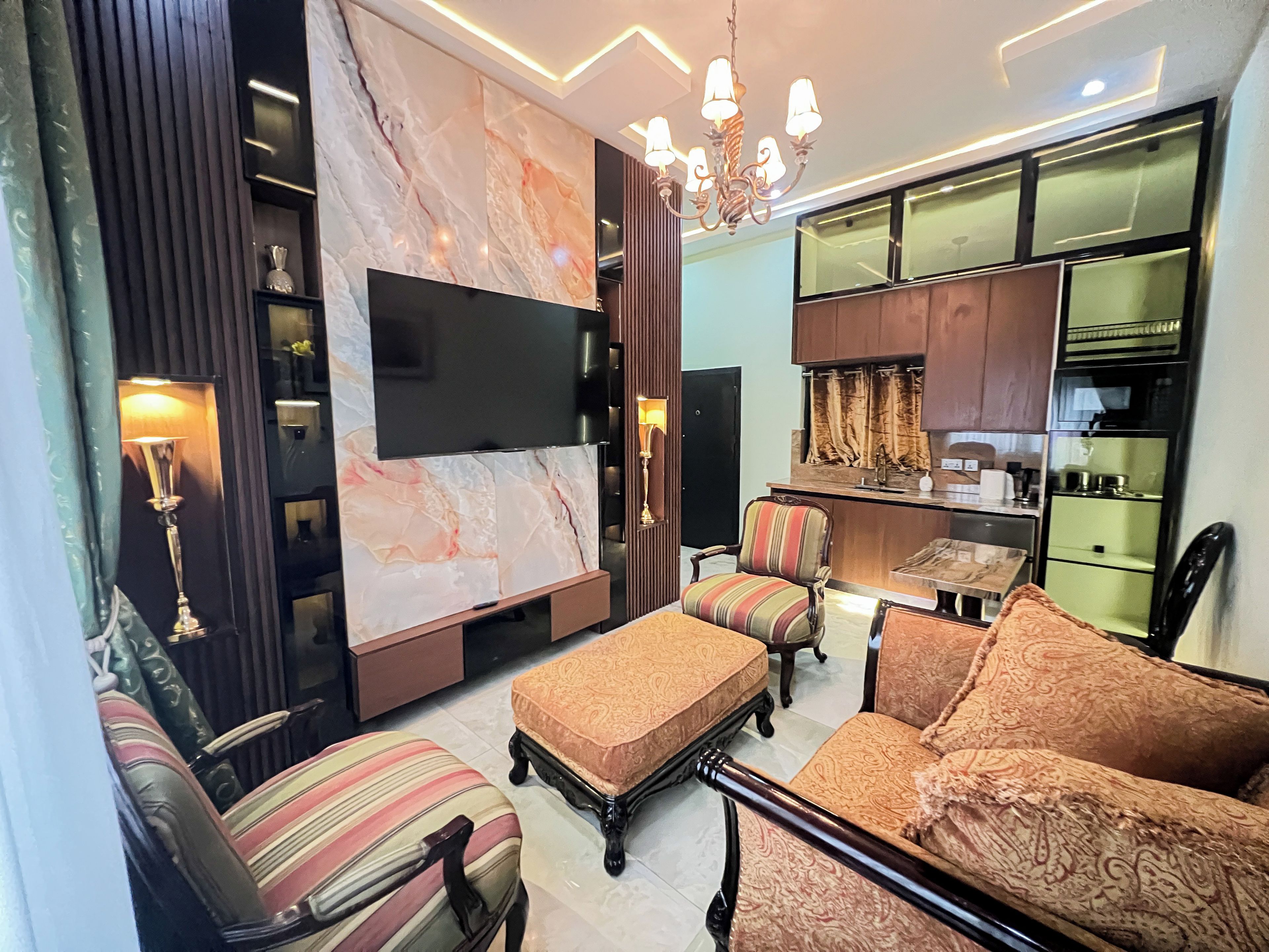 A modern living room with a flat-screen TV, patterned sofas, a dining area, and a kitchen with wooden cabinets.