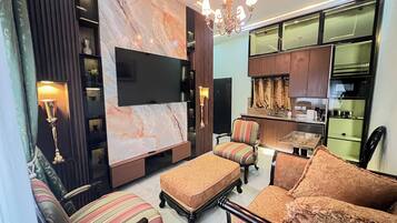 A modern living room with a flat-screen TV, patterned sofas, a dining area, and a kitchen with wooden cabinets.